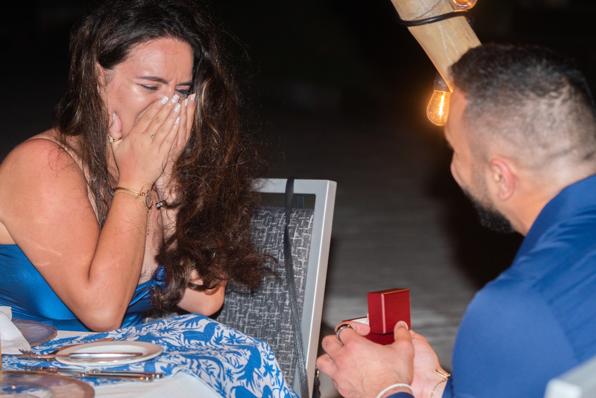 A man holding a ring box while his partner reacts with emotion.